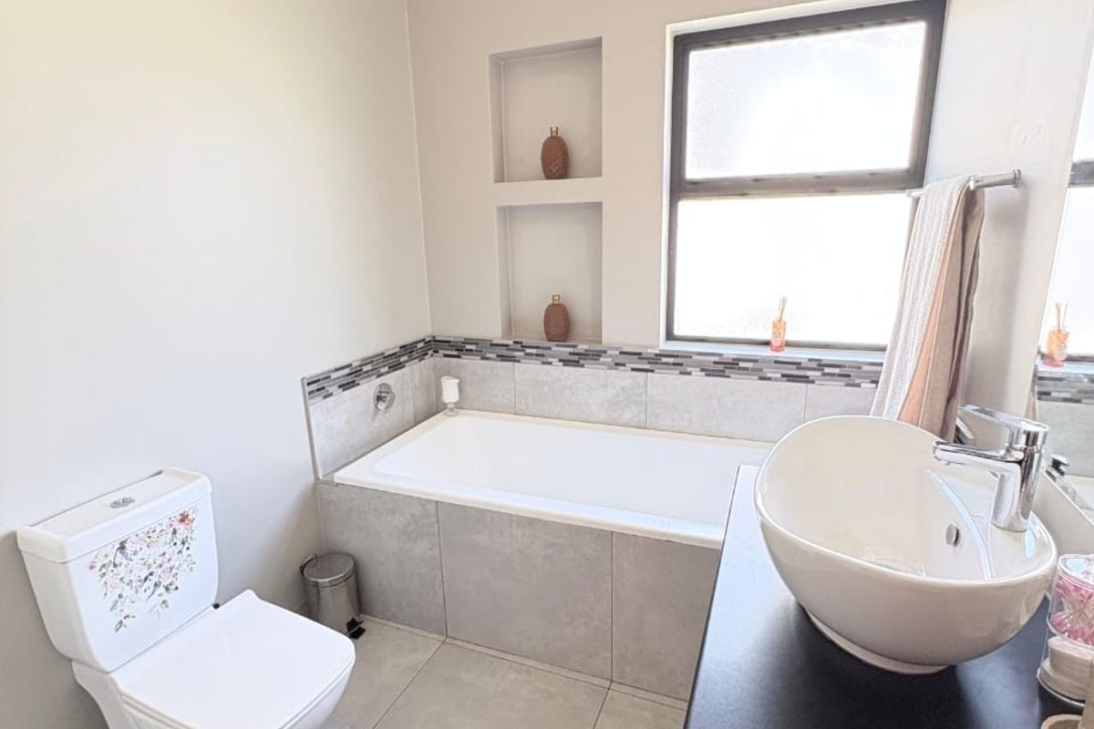 Modern bathroom featuring a built-in bathtub with tiled surround, recessed wall niches, a vessel sink on a vanity cabinet, and a toilet.