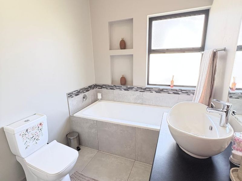 Modern bathroom featuring a built-in bathtub with tiled surround, recessed wall niches, a vessel sink on a vanity cabinet, and a toilet.