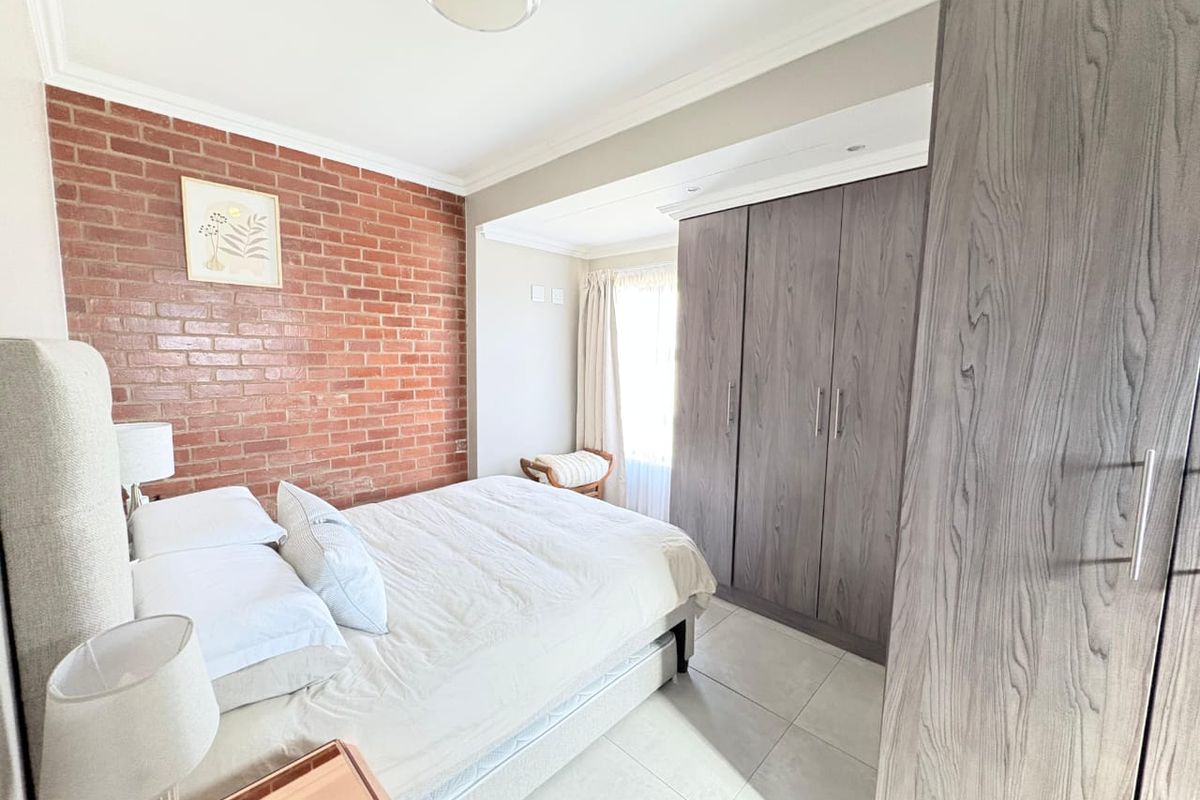 A well-maintained bedroom featuring a striking exposed brick feature wall, neutral tiled flooring, and ample built-in cupboard storage.