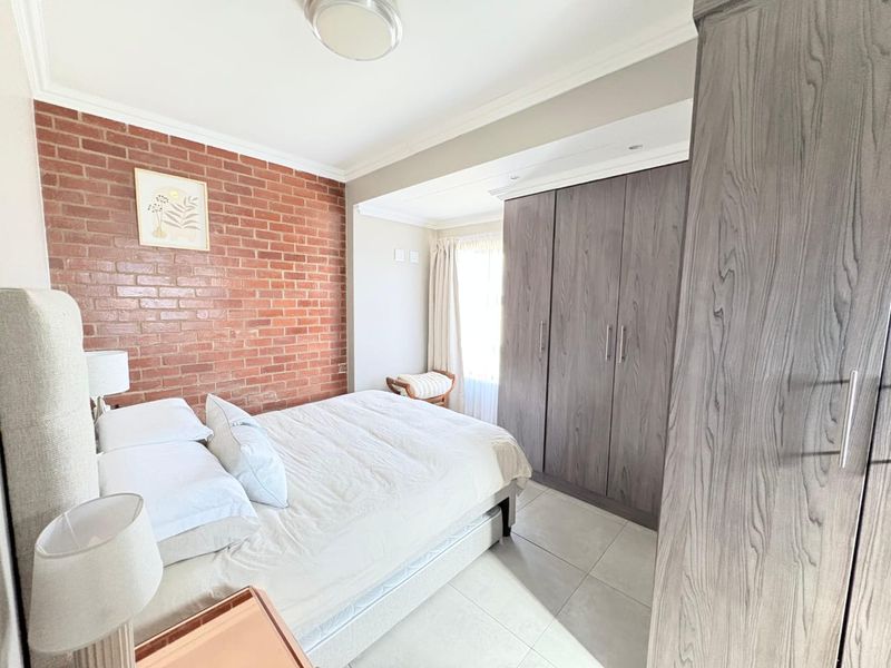 A well-maintained bedroom featuring a striking exposed brick feature wall, neutral tiled flooring, and ample built-in cupboard storage.