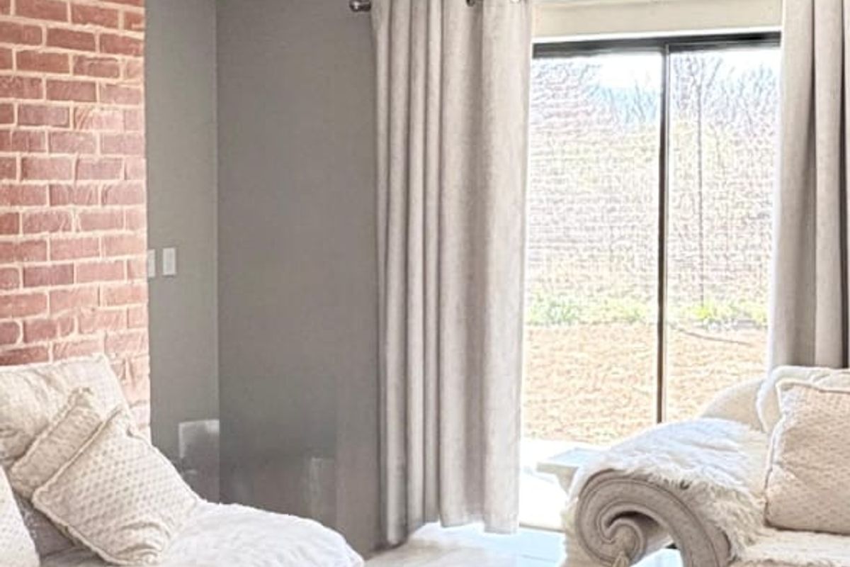 A bright living room featuring large format floor tiles, an exposed brick feature wall, and a sliding glass door providing access to the outdoors.