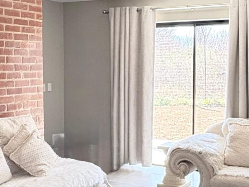 A bright living room featuring large format floor tiles, an exposed brick feature wall, and a sliding glass door providing access to the outdoors.