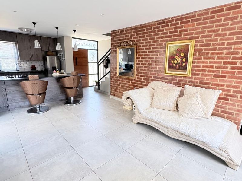 Spacious open-plan living area featuring a modern kitchen with island, tiled floors, and a striking exposed brick feature wall leading to the entrance.
