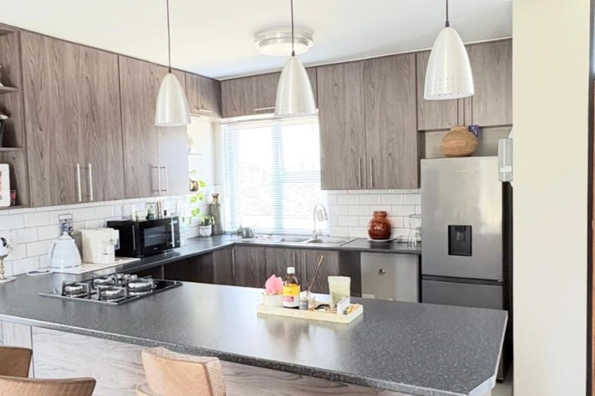 Modern kitchen featuring wood-grain cabinetry, stone countertops, a gas hob, and a breakfast bar with pendant lighting.