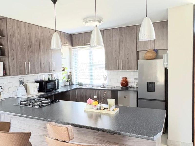 Modern kitchen featuring wood-grain cabinetry, stone countertops, a gas hob, and a breakfast bar with pendant lighting.