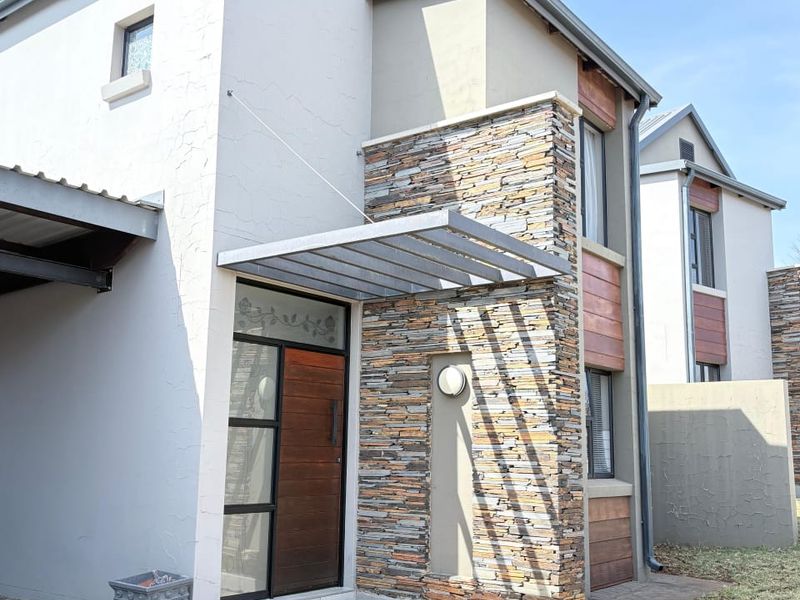 Modern townhouse exterior featuring stone cladding, a metal entrance canopy, and a timber front door with a paved driveway and walkway.