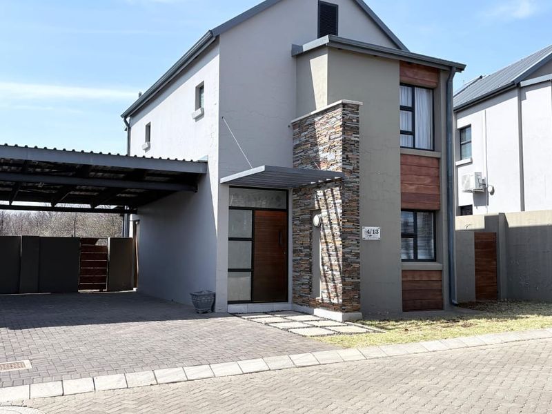 Modern townhouse exterior featuring a combination of stone and timber cladding, a paved driveway, and an integrated carport.