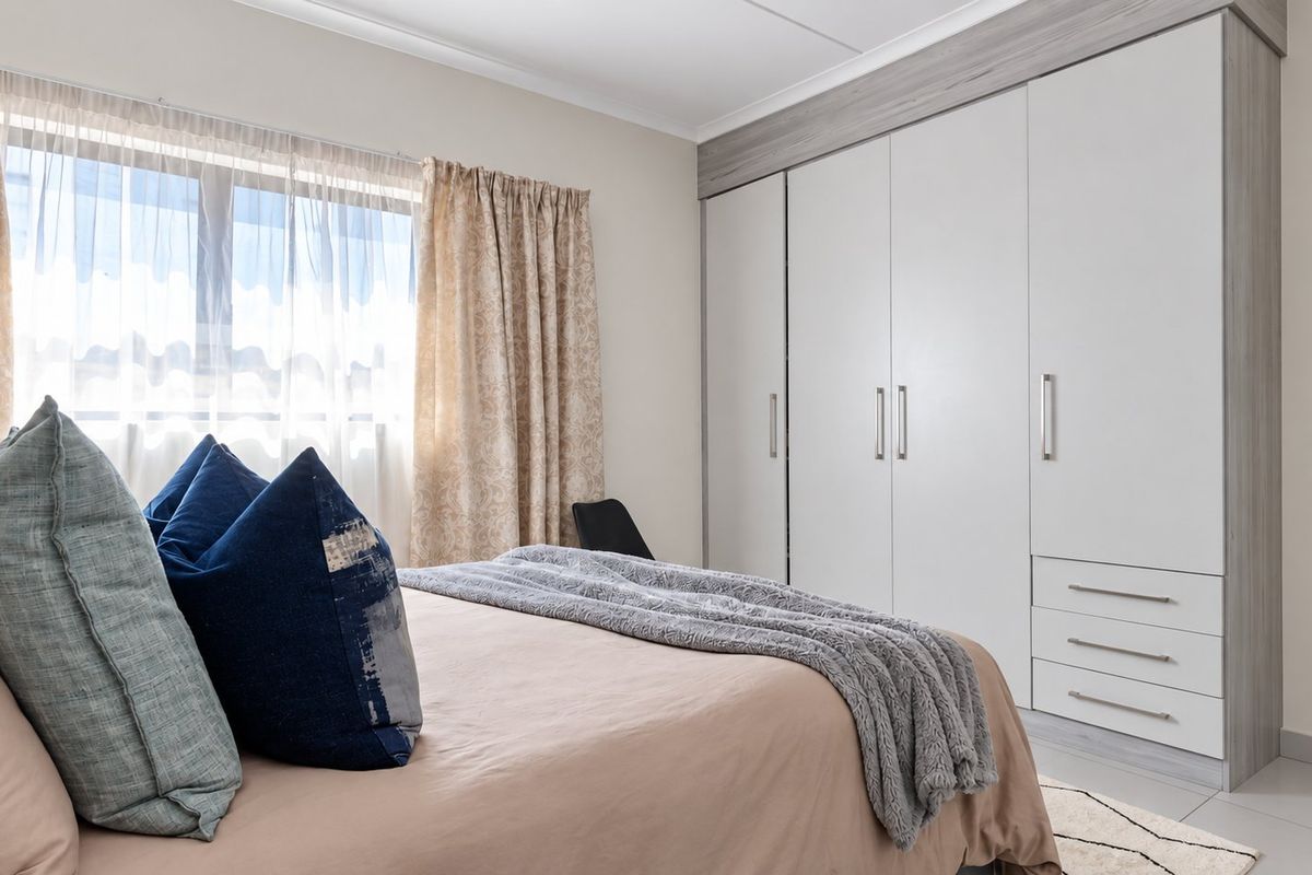 A well-maintained bedroom featuring neutral tiled flooring, cove cornicing, and extensive built-in cupboards with modern finishes.