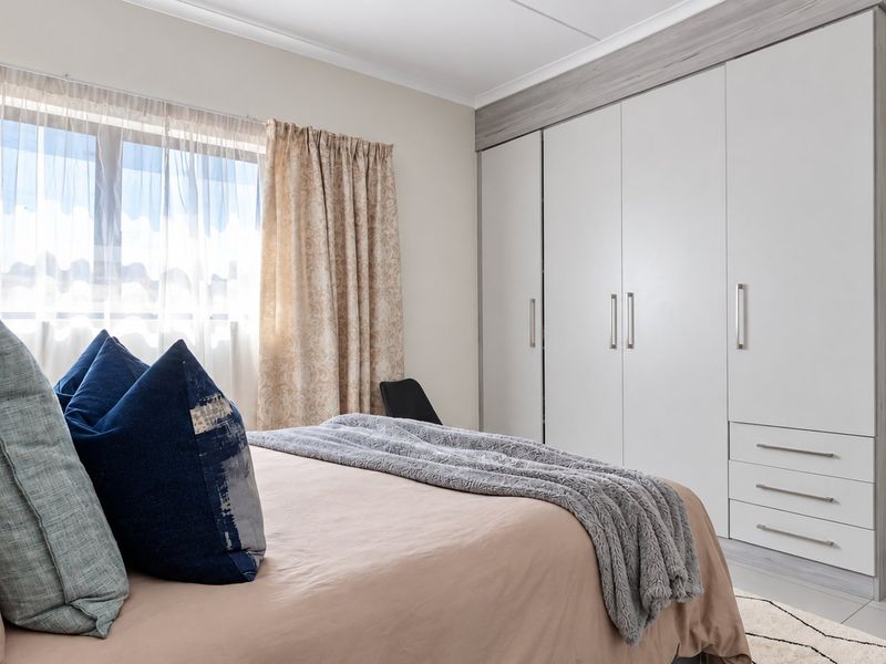 A well-maintained bedroom featuring neutral tiled flooring, cove cornicing, and extensive built-in cupboards with modern finishes.