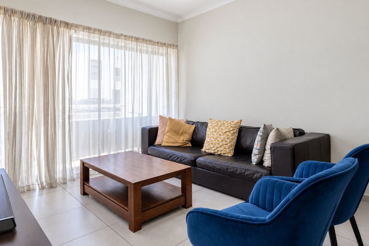 A bright living room featuring neutral tiled flooring and a large sliding glass door with sheer curtains, providing ample natural light.
