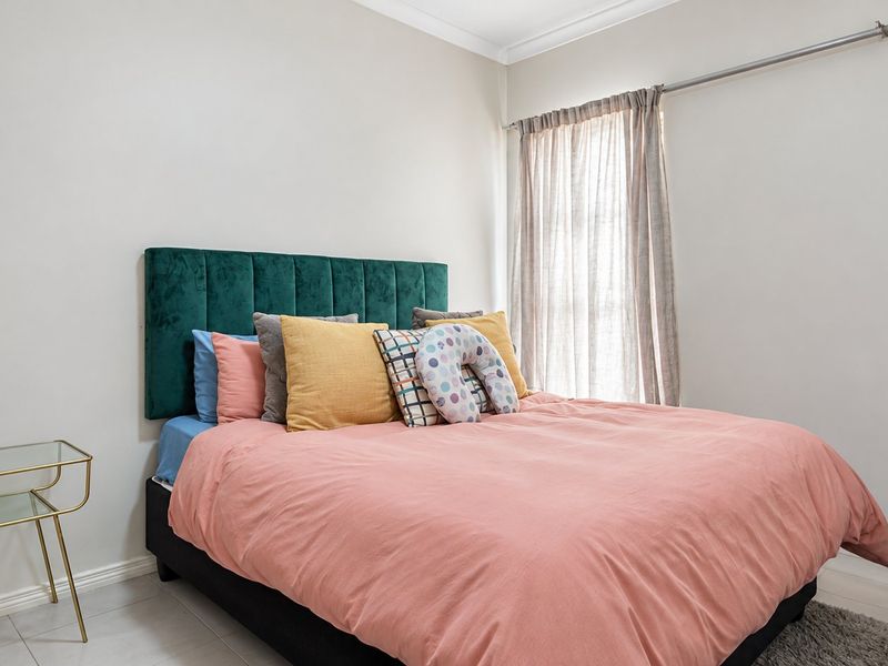 A well-maintained bedroom featuring neutral wall finishes, tiled flooring, and a window fitted with a curtain rod.