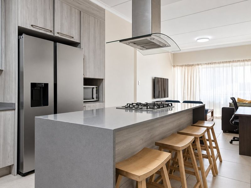 Modern open-plan kitchen featuring sleek cabinetry, stone countertops, a central island with a gas hob, and integrated appliances, flowing into the living area.