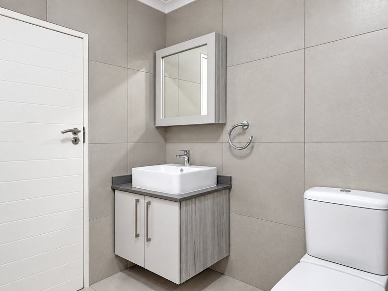 Modern bathroom featuring a wall-mounted vanity with vessel sink, mirrored medicine cabinet, and neutral large-format wall tiles.