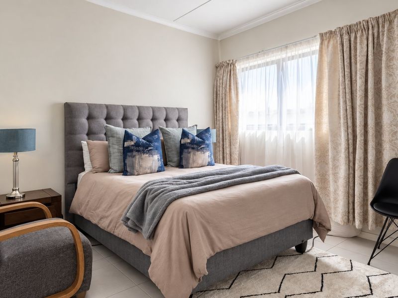 A well-lit bedroom featuring neutral wall tones, tiled flooring, and classic cove cornice detailing, providing a comfortable and functional living space.