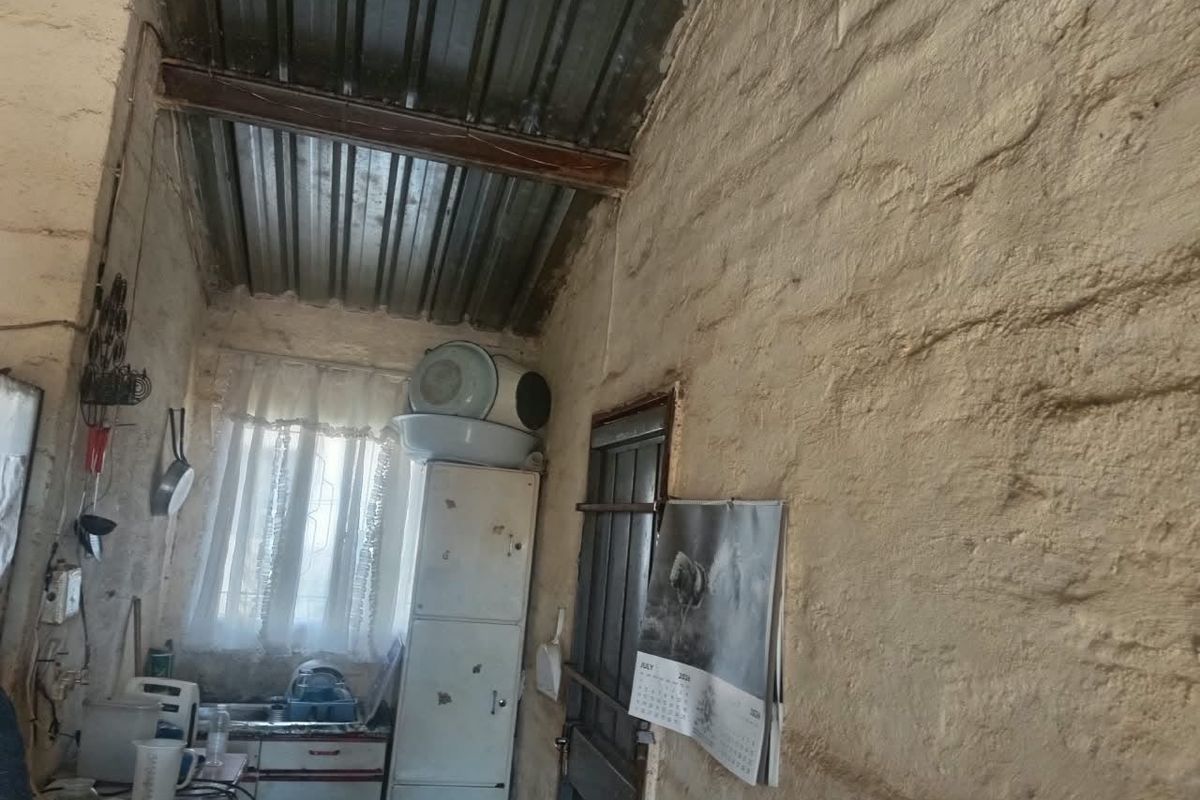 A rustic kitchen area featuring exposed masonry walls, a corrugated metal ceiling, and basic fitted cabinetry with a sink.