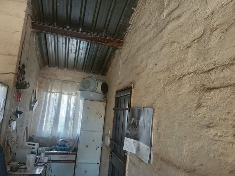 A rustic kitchen area featuring exposed masonry walls, a corrugated metal ceiling, and basic fitted cabinetry with a sink.