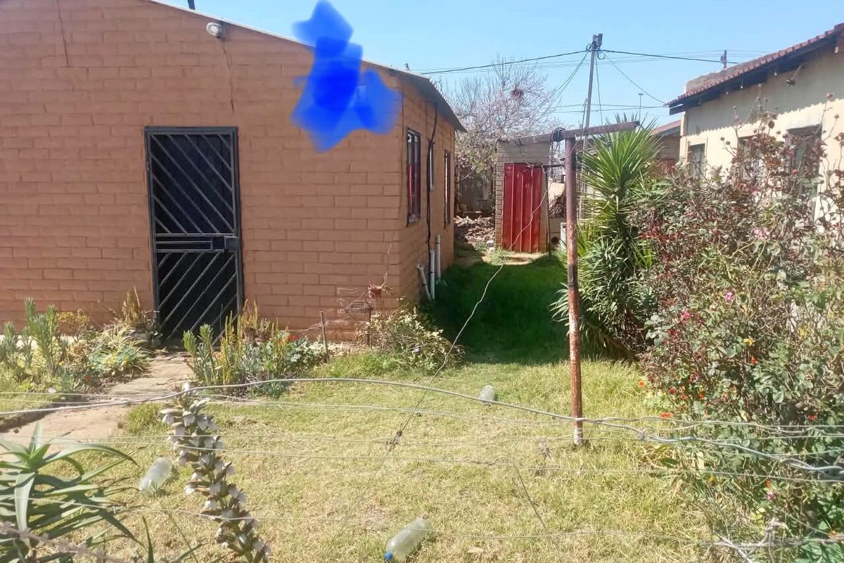 Rear view of a brick house featuring a security gate, solar water heater, and a small garden area with a metal washing line.