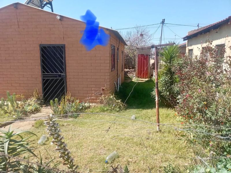 Rear view of a brick house featuring a security gate, solar water heater, and a small garden area with a metal washing line.