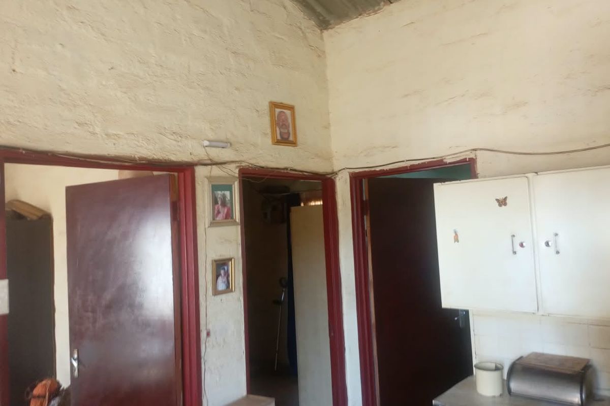 A hallway area featuring textured masonry walls, exposed corrugated metal ceiling, and built-in cabinetry, showing signs of significant wear and dated finishes.
