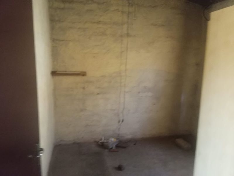 An unfinished utility space featuring exposed brick walls and visible electrical wiring, requiring significant renovation and finishing work.