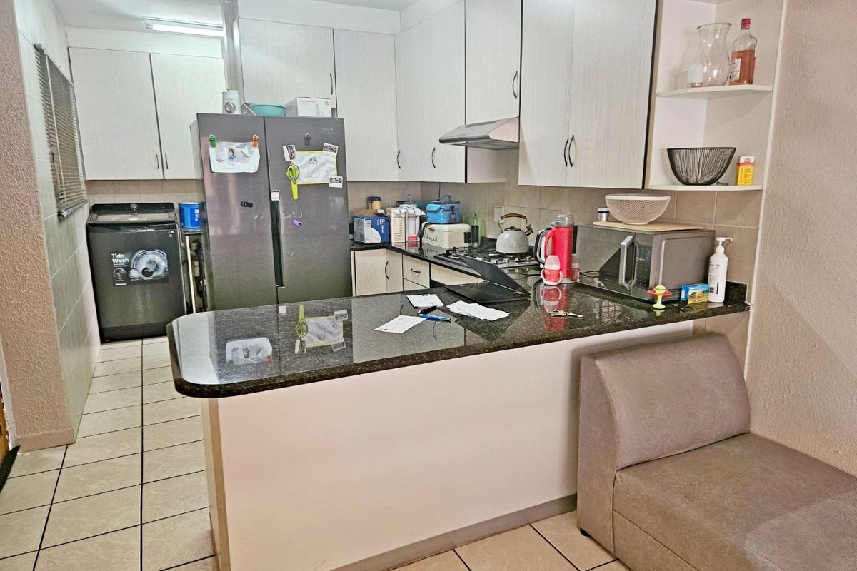 Functional kitchen featuring granite countertops, built-in cabinetry, a gas hob with extractor fan, and a breakfast bar, with tiled flooring throughout.