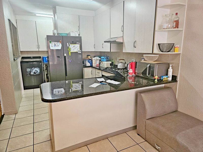Functional kitchen featuring granite countertops, built-in cabinetry, a gas hob with extractor fan, and a breakfast bar, with tiled flooring throughout.