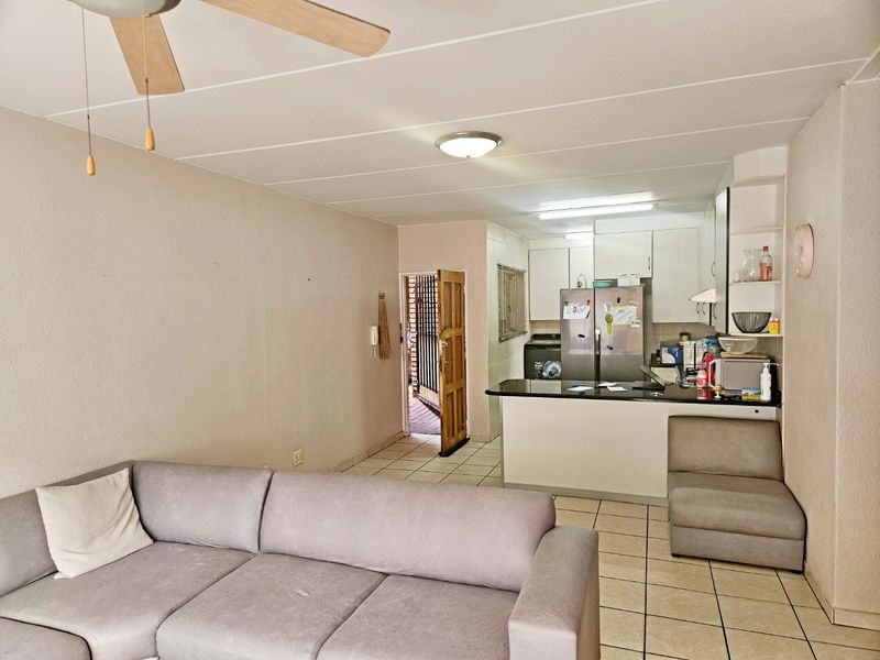 Open-plan living area featuring a kitchen with built-in cabinetry and a breakfast counter, leading to an exterior entrance with a security gate.