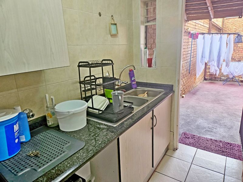 A functional scullery area featuring a double bowl sink, stone countertops, and tiled finishes, with direct access to an outdoor drying area.