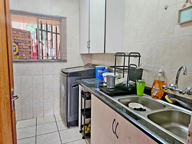 A functional laundry room featuring tiled walls and flooring, built-in cabinetry, granite countertops, and a double basin stainless steel sink.