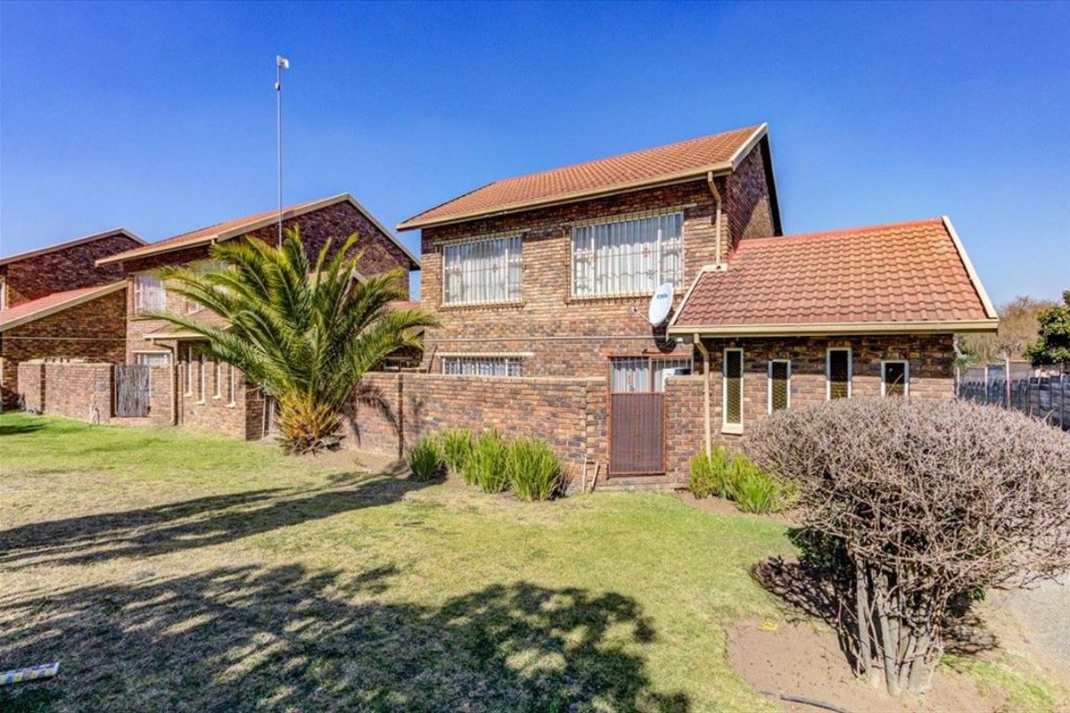 Rear view of a double-story face brick townhouse featuring a tiled roof, security bars on windows, and a private garden area.