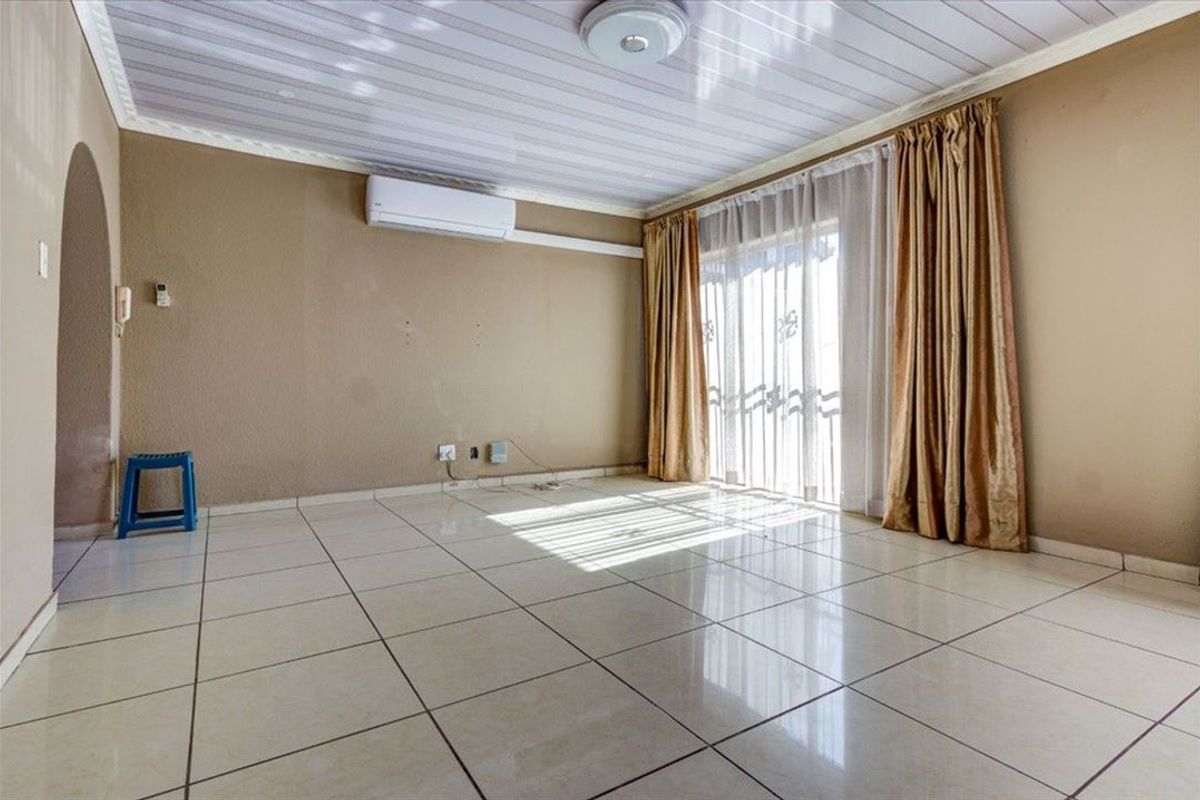 Spacious living area featuring neutral tiled flooring, a wall-mounted air conditioning unit, and sliding glass doors providing access to the exterior.