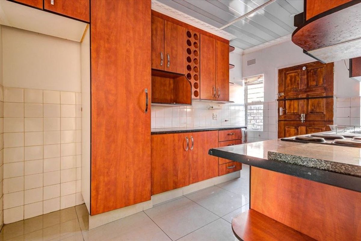 A functional kitchen featuring wood-look laminate cabinetry, granite countertops, and tiled finishes, offering a practical layout ready for modern updates.