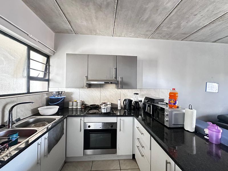 A functional kitchen featuring granite countertops, built-in oven and hob, tiled backsplash, and an industrial-style exposed concrete ceiling.