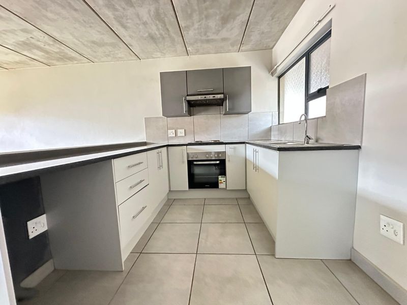Modern kitchen featuring built-in cabinetry, integrated oven and hob, tiled backsplash, and an industrial-style exposed concrete ceiling.