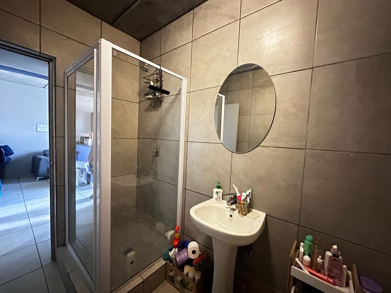 A functional bathroom featuring a glass shower enclosure, pedestal basin, and neutral wall tiling.