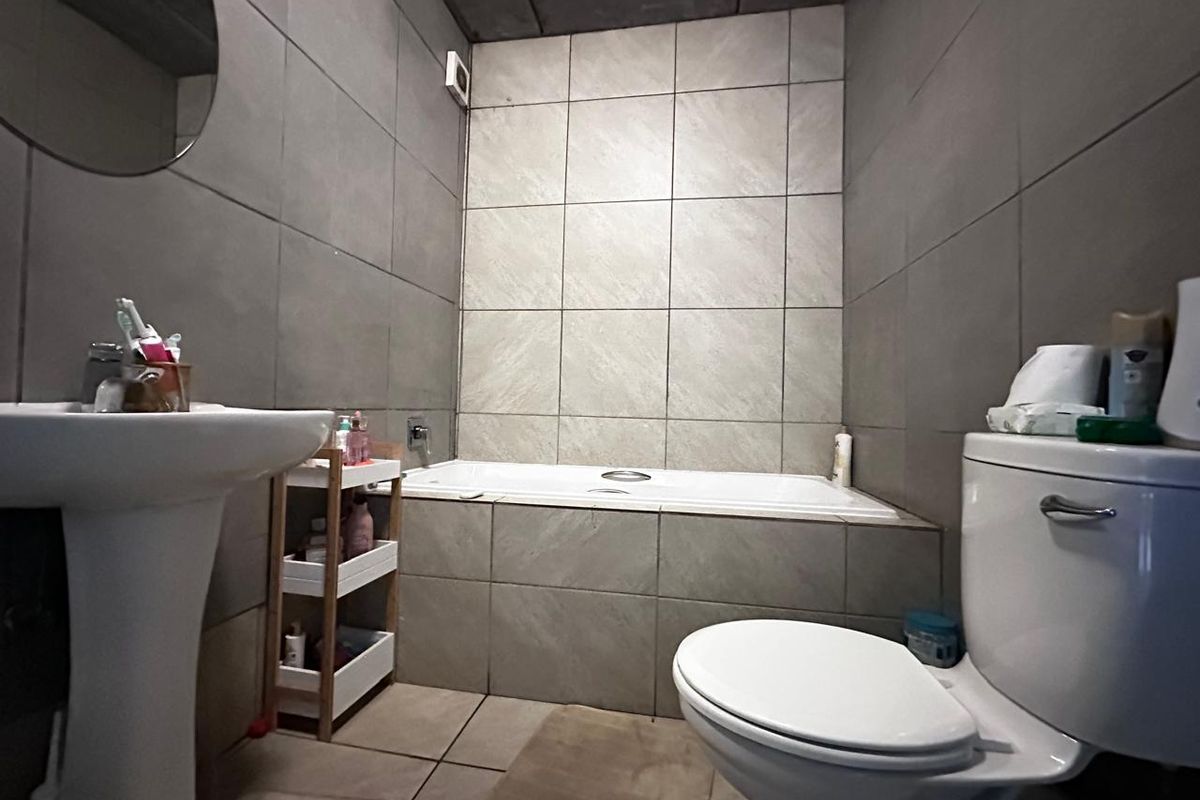 A functional bathroom featuring a pedestal basin, a built-in bathtub with tiled surround, and neutral ceramic wall and floor tiling.