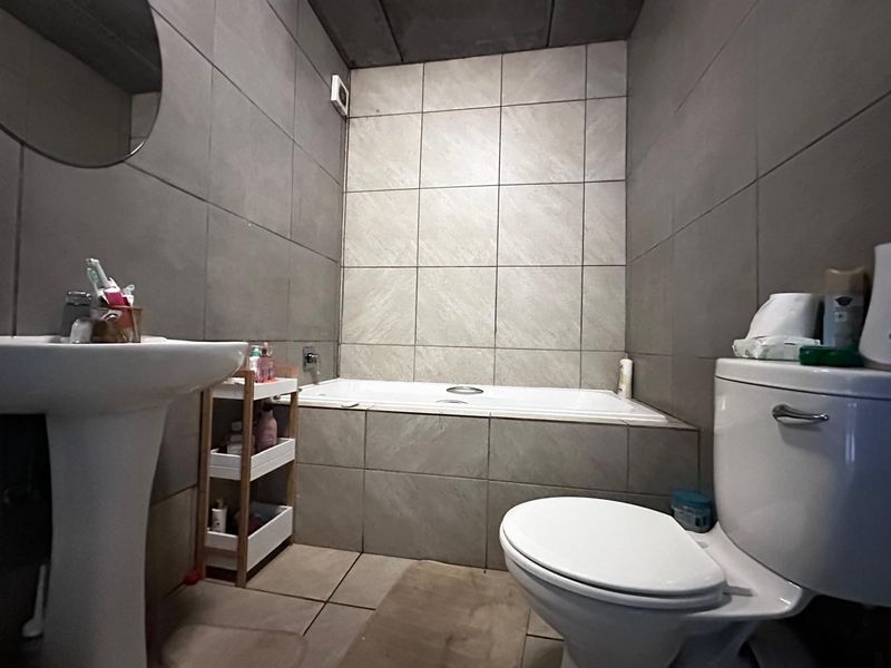 A functional bathroom featuring a pedestal basin, a built-in bathtub with tiled surround, and neutral ceramic wall and floor tiling.