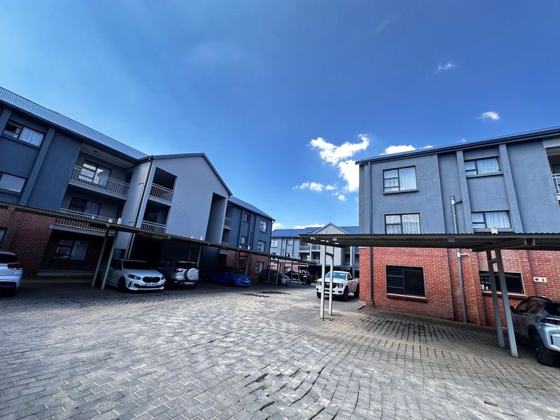 Exterior view of an apartment complex featuring paved parking areas, covered carports, and multi-story buildings with a mix of brick and painted plaster finishes.