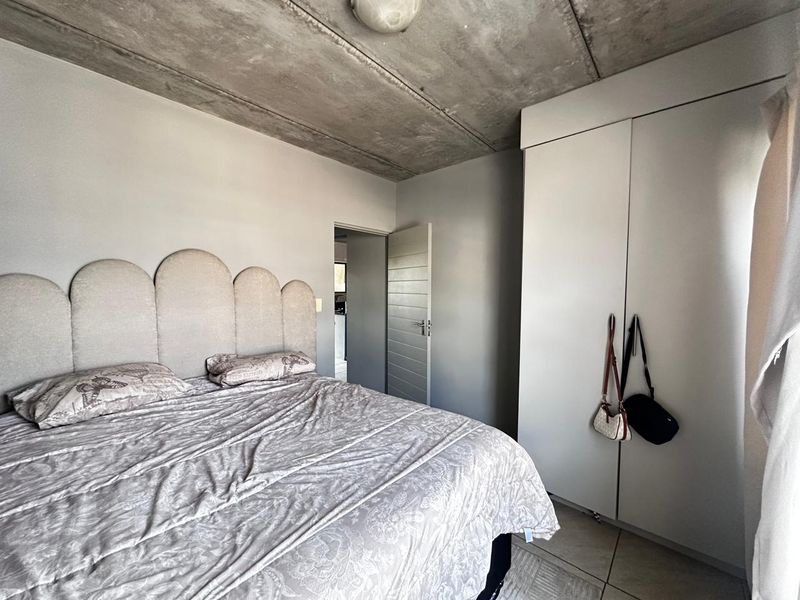 A bedroom featuring an exposed concrete ceiling, tiled flooring, and a built-in wardrobe with a neutral color palette.