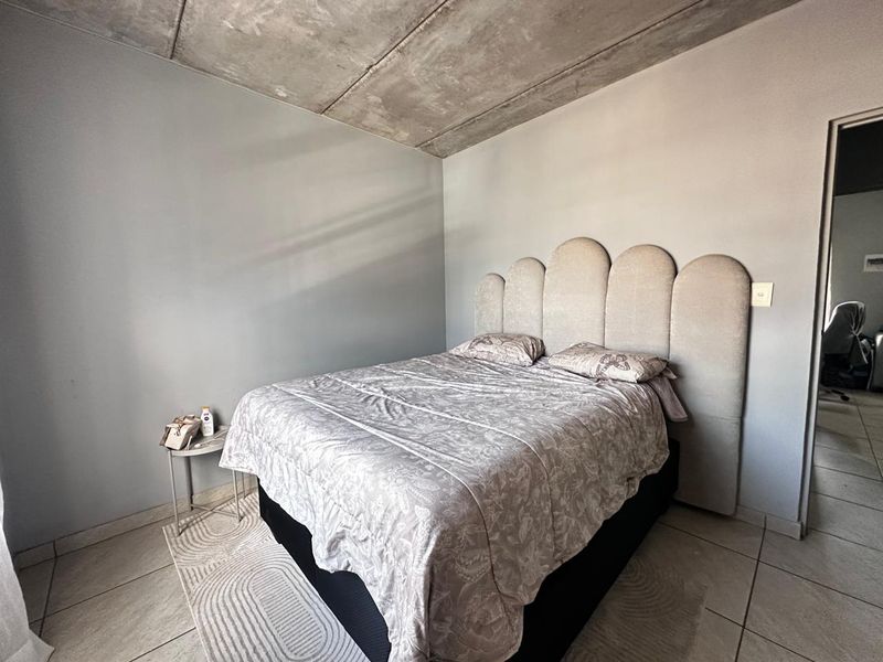 A bedroom featuring an industrial-style exposed concrete ceiling and neutral tiled flooring, providing a modern foundation for personalization.