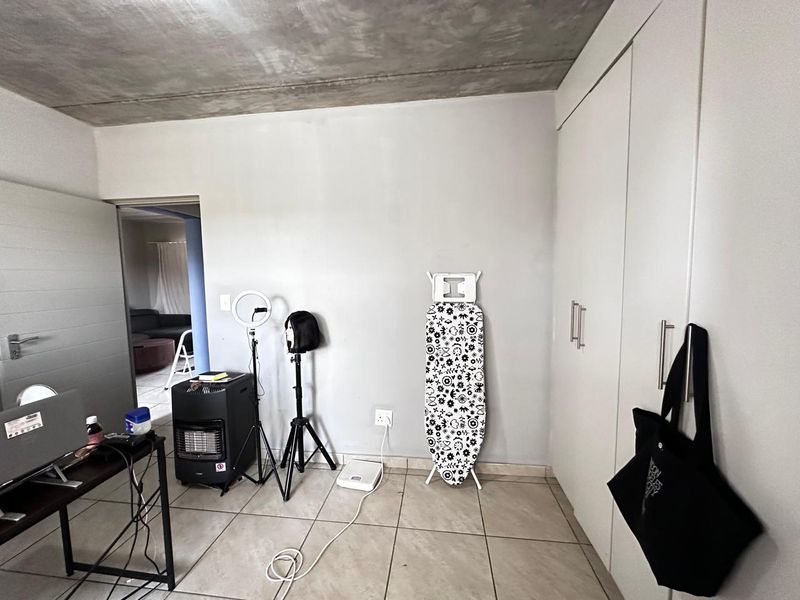 A bedroom featuring built-in cupboards, tiled flooring, and an exposed concrete ceiling, offering a functional space with potential for modern updates.