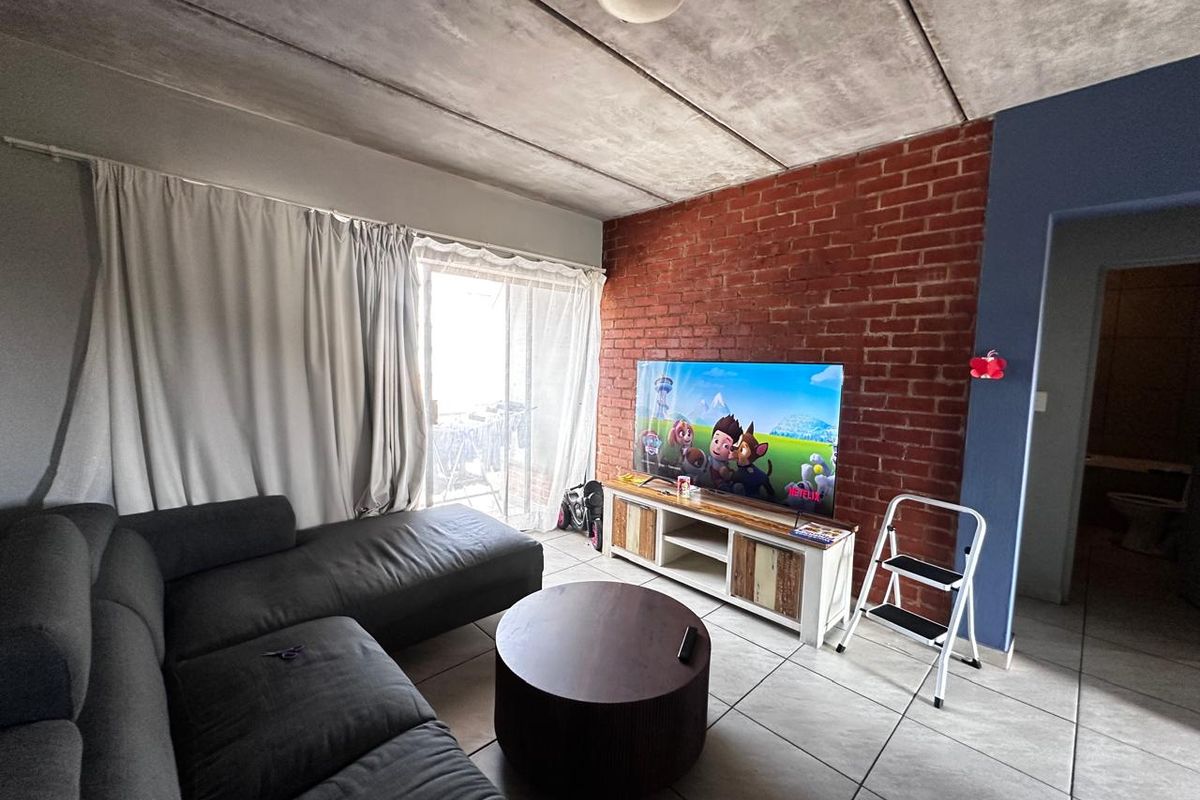 Living room featuring an exposed concrete ceiling, a rustic brick feature wall, and tiled flooring with access to an outdoor area.