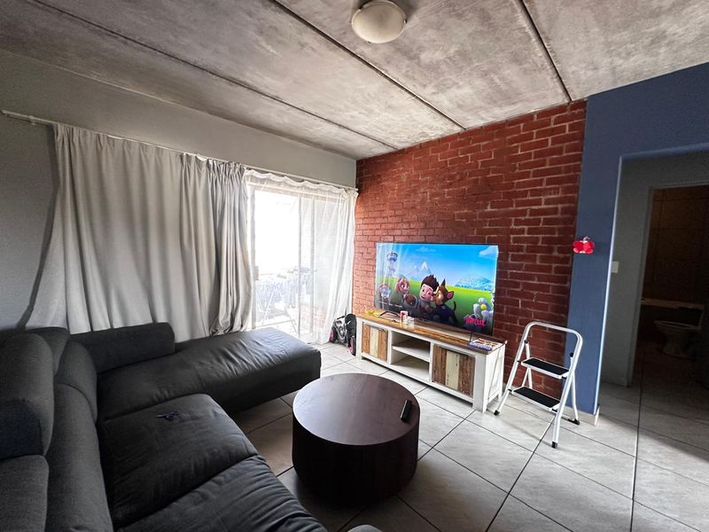 Living room featuring an exposed concrete ceiling, a rustic brick feature wall, and tiled flooring with access to an outdoor area.