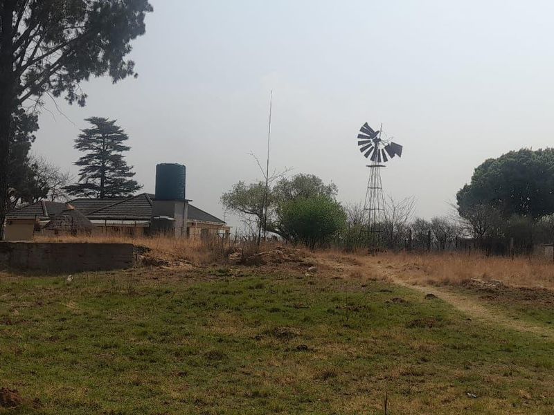 A wide view of the farm grounds featuring a traditional windmill, water tank, and the rear elevation of the main dwelling.