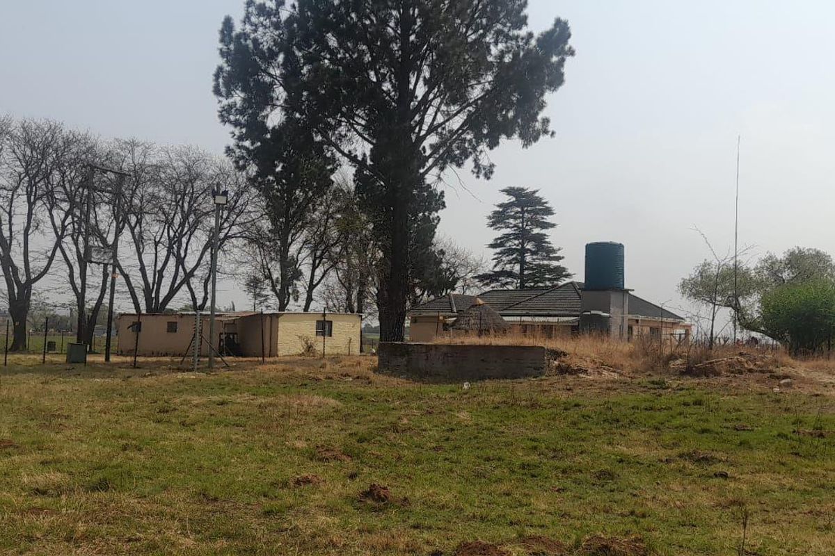 A wide view of the farm property featuring a windmill, water storage tank, concrete reservoir, and an outbuilding set within a rural landscape.