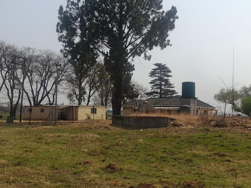 A wide view of the farm property featuring a windmill, water storage tank, concrete reservoir, and an outbuilding set within a rural landscape.