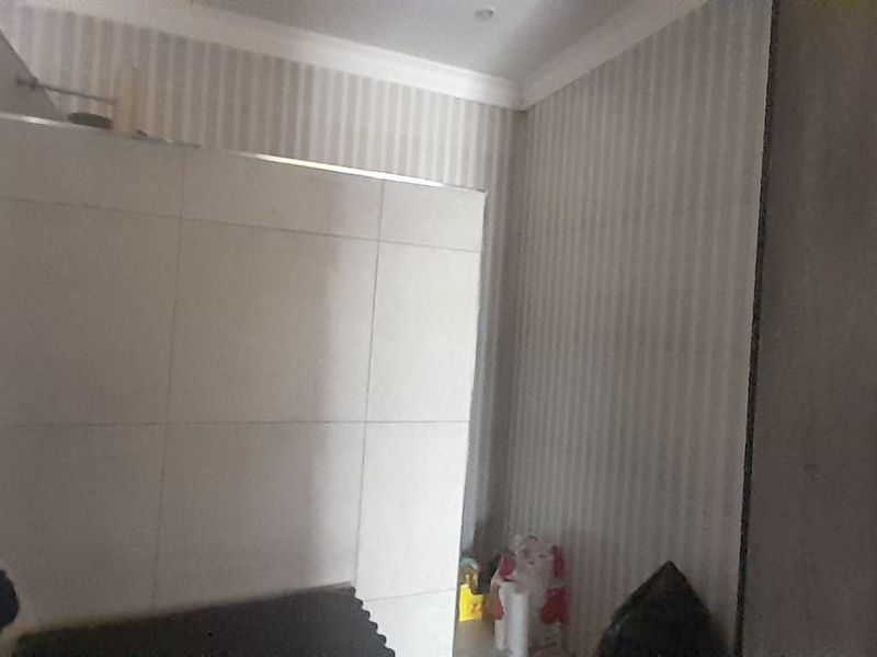A bathroom featuring a tiled shower enclosure, built-in cabinetry, and decorative wallpaper, offering a functional space with potential for modern updates.