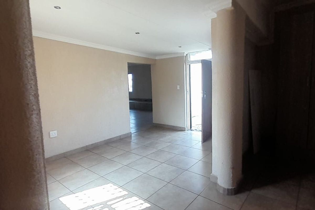 An open-plan living area featuring tiled flooring, a structural column, and built-in storage cupboards, offering a neutral and versatile space.