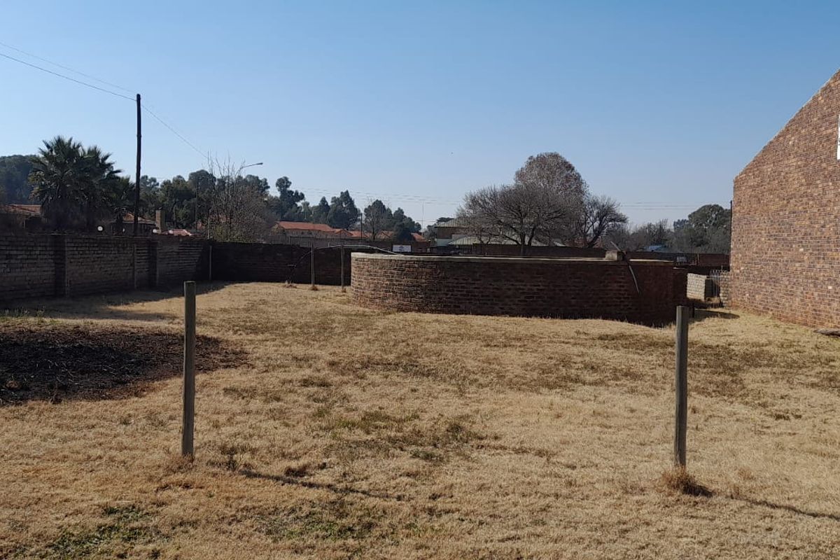 A large, open outdoor area featuring a brick boundary wall, a circular brick feature, and an adjacent brick storage building.