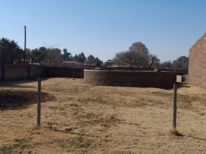 A large, open outdoor area featuring a brick boundary wall, a circular brick feature, and an adjacent brick storage building.